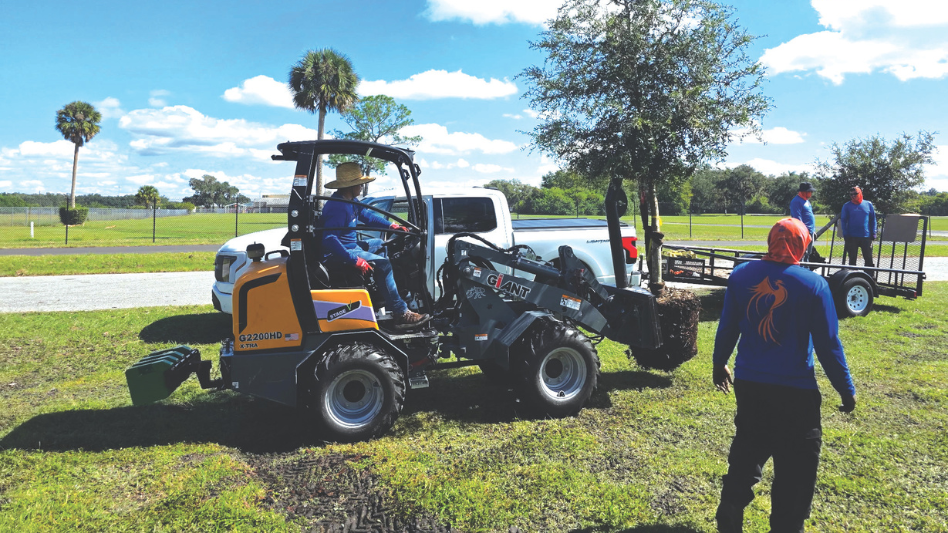 Landscape employees standing beside large equipment