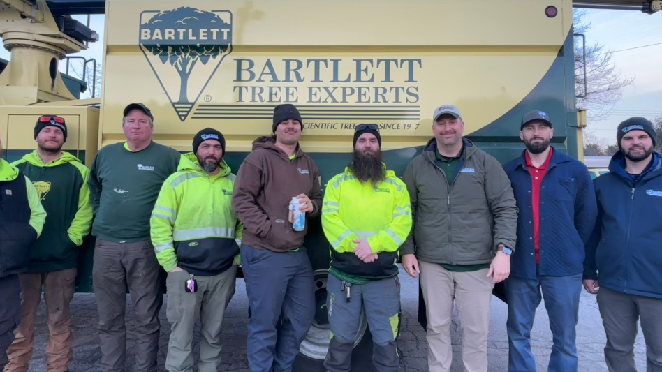 Bartlett Tree Experts employees stand in front of the logo